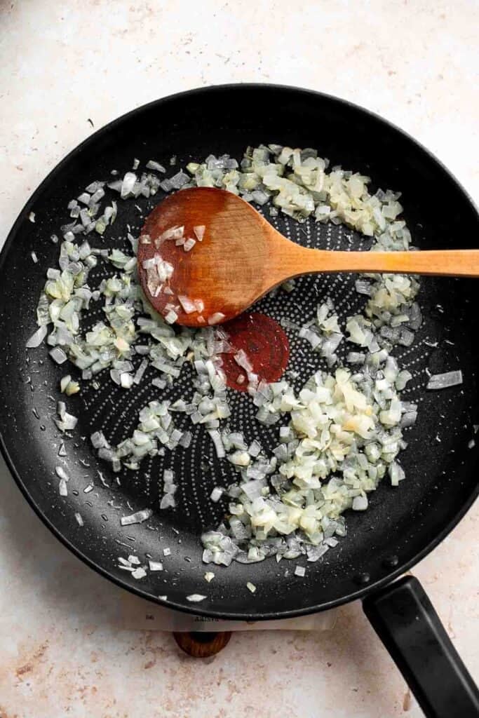 Onion and garlic sautéing in a skillet with a wooden spoon