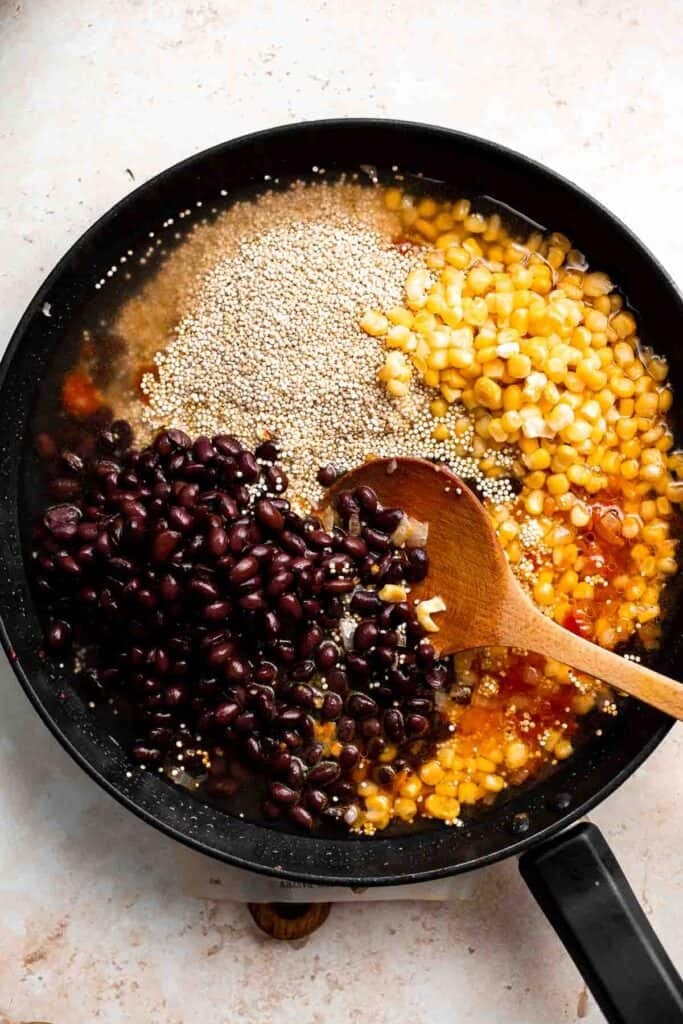 Quinoa, black beans, and corn being combined in a skillet for the stuffed pepper filling