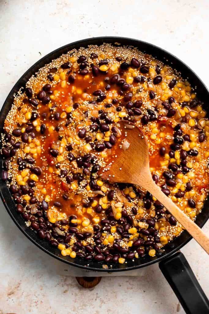 Overhead view of quinoa filling simmering in a skillet with a wooden spoon