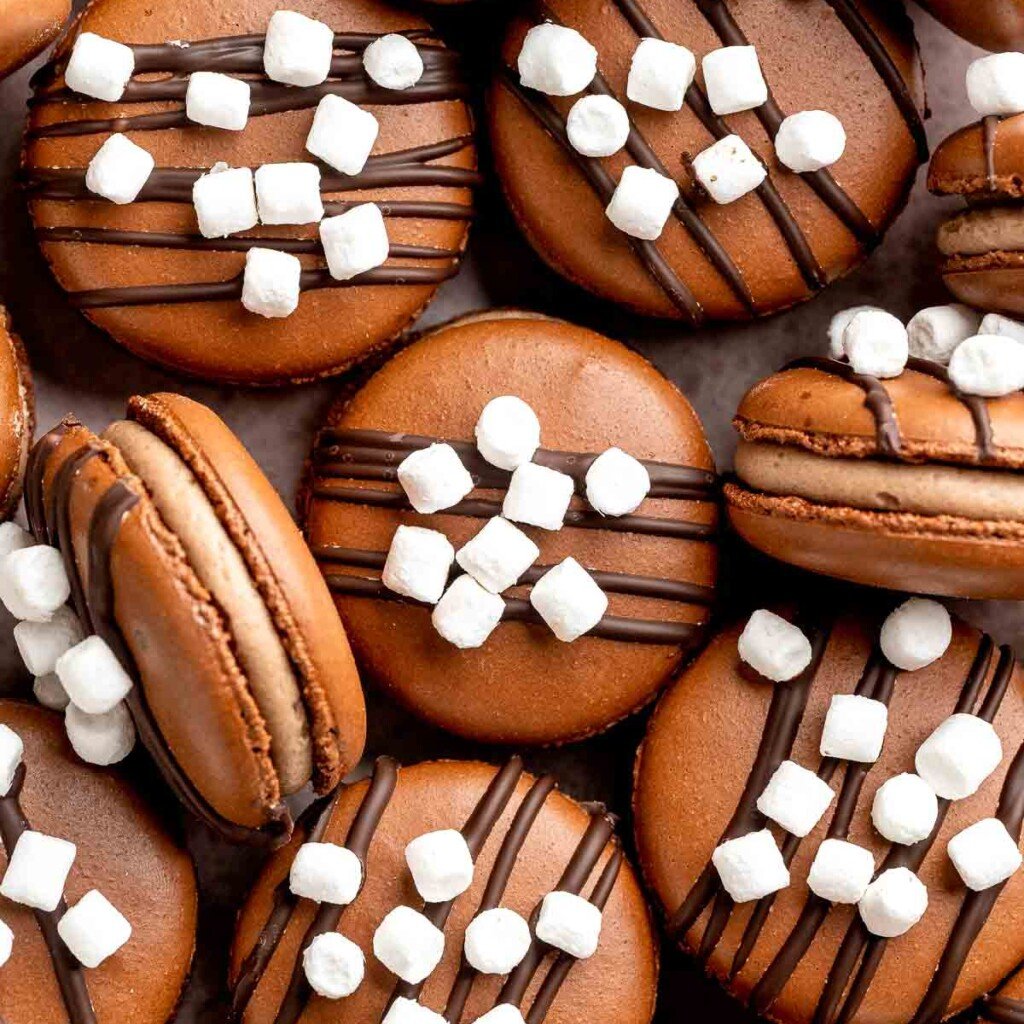 Hot chocolate macarons with cocoa shells and fluffy marshmallow filling. A cozy winter treat perfect for holiday baking and festive cookie trays. | aheadofthyme.com
