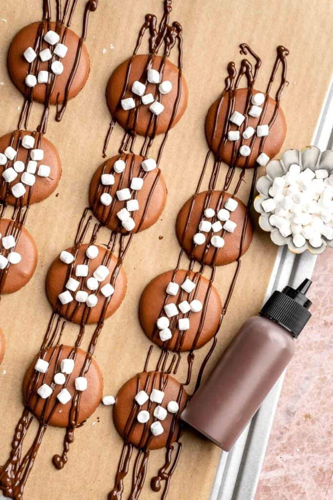 Hot chocolate macarons with cocoa shells and fluffy marshmallow filling. A cozy winter treat perfect for holiday baking and festive cookie trays. | aheadofthyme.com