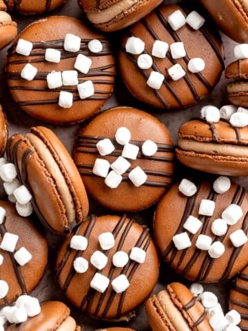 Hot chocolate macarons with cocoa shells and fluffy marshmallow filling. A cozy winter treat perfect for holiday baking and festive cookie trays. | aheadofthyme.com