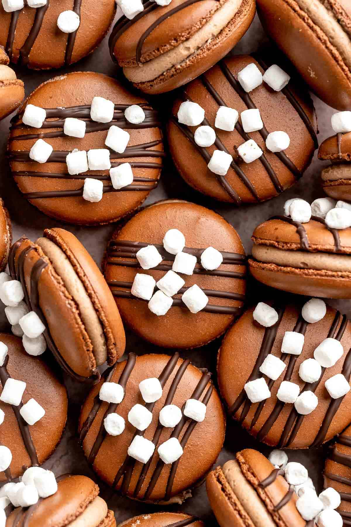 Hot chocolate macarons with cocoa shells and fluffy marshmallow filling. A cozy winter treat perfect for holiday baking and festive cookie trays. | aheadofthyme.com