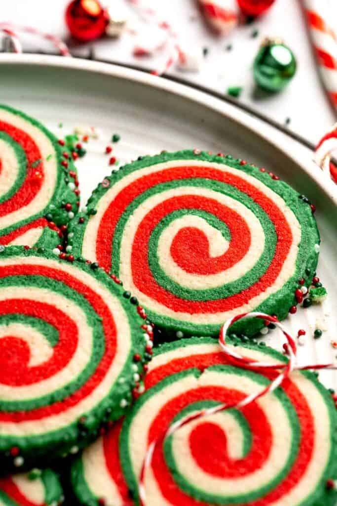 Peppermint pinwheel cookies with red, green, and white swirled dough rolled in festive sprinkles. A fun slice and bake Christmas cookie. | aheadofthyme.com
