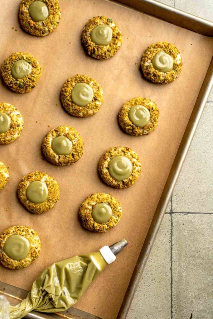 Buttery pistachio thumbprint cookies filled with pistachio white chocolate ganache that bake into elegant, nutty treats perfect for gifting or any occasion. | aheadofthyme.com