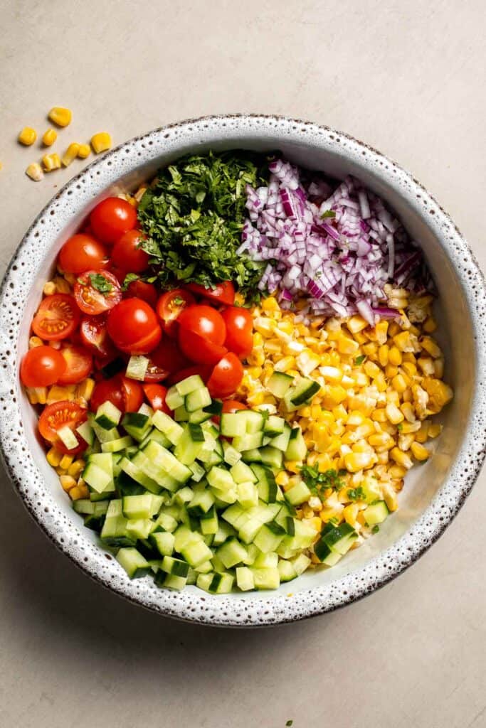 Corn, cherry tomatoes, cucumber, and red onion combined in a serving bowl.