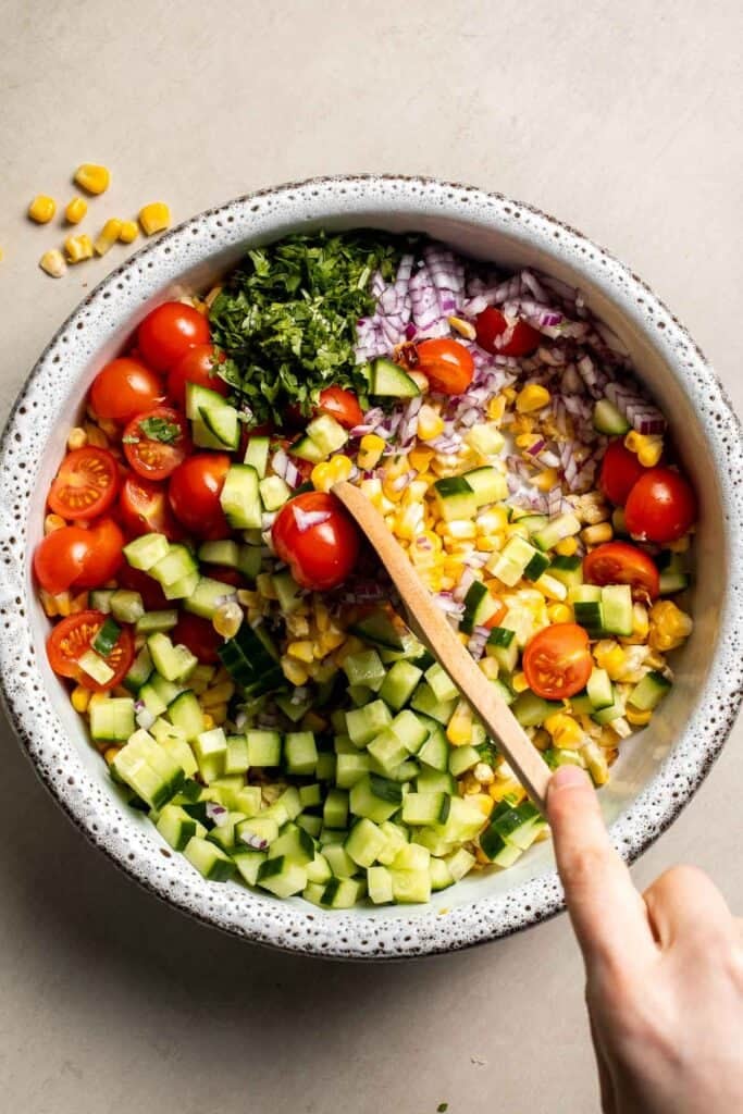 Avocado corn salad being tossed together in a large bowl.