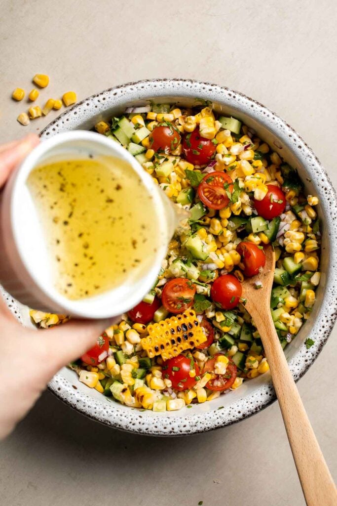 Pouring lime dressing over avocado corn salad.