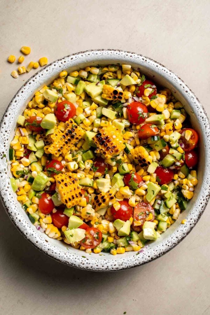 Fresh avocado corn salad with tomatoes, cucumber, cilantro, and lime dressing.