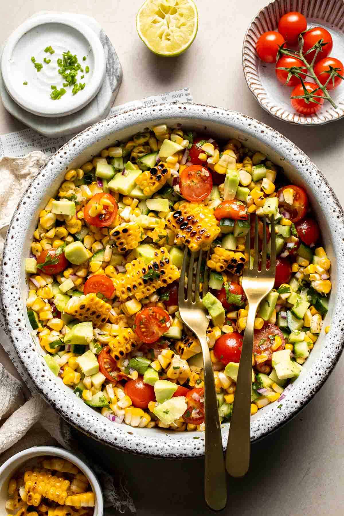 Avocado corn salad with grilled corn, avocado, cherry tomatoes, cucumber, red onion, cilantro, and lime dressing.