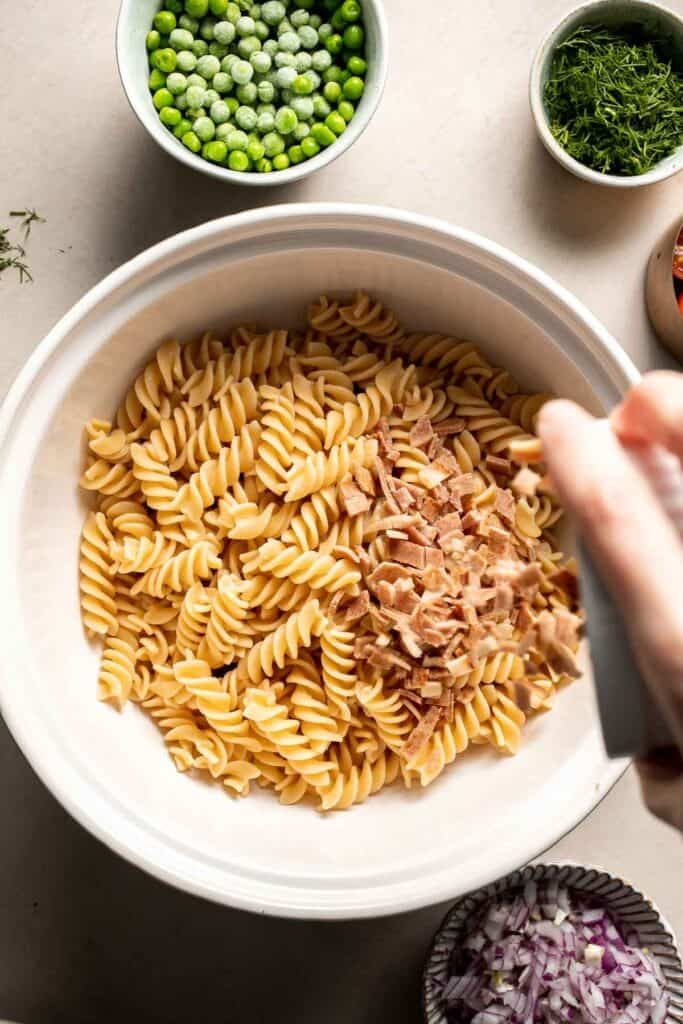 Crispy bacon being added to cooked pasta.