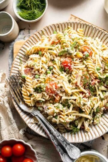 Bacon ranch pasta salad with crispy bacon, cheddar cheese, peas, tomatoes, and creamy ranch dressing.