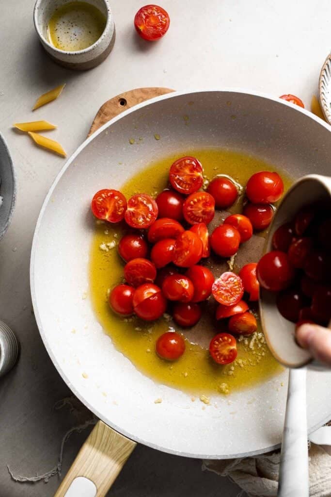Cherry tomatoes being added to a skillet with garlic and olive oil.