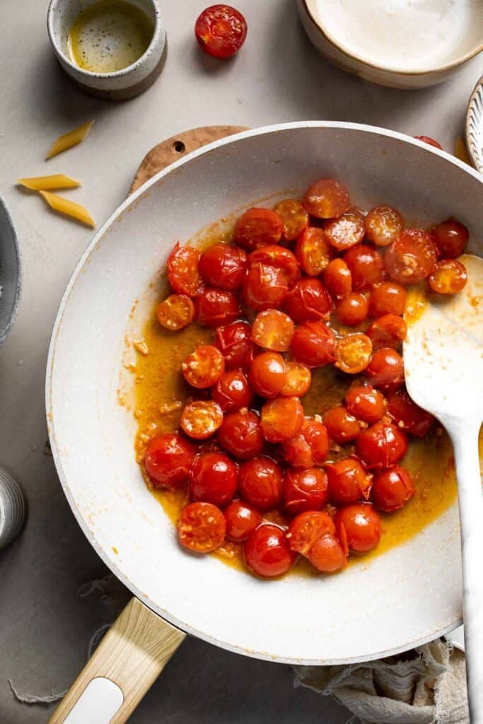 Cooked pasta being added to sautéed tomatoes in a skillet.