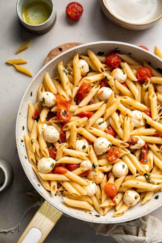 Finished Caprese pasta with melted mozzarella and fresh basil in a skillet.