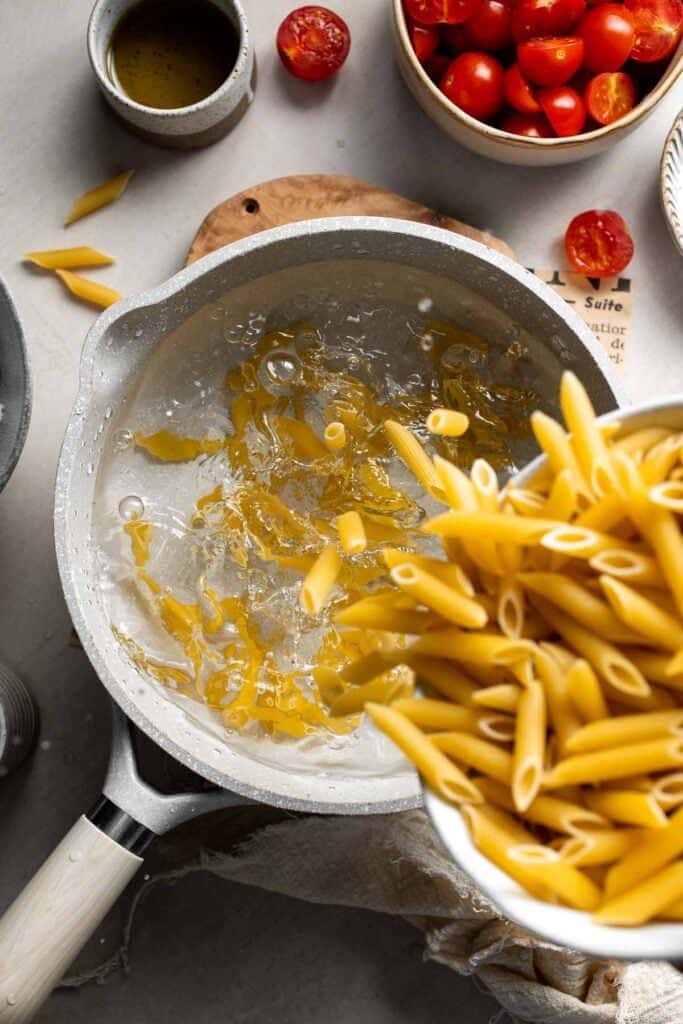 Penne pasta being added to boiling water in a large pot.