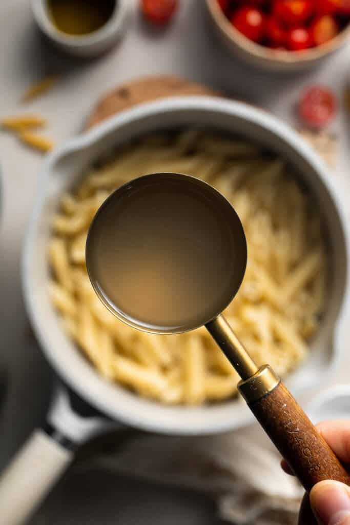 Reserved pasta water being scooped from the pot before draining the pasta.