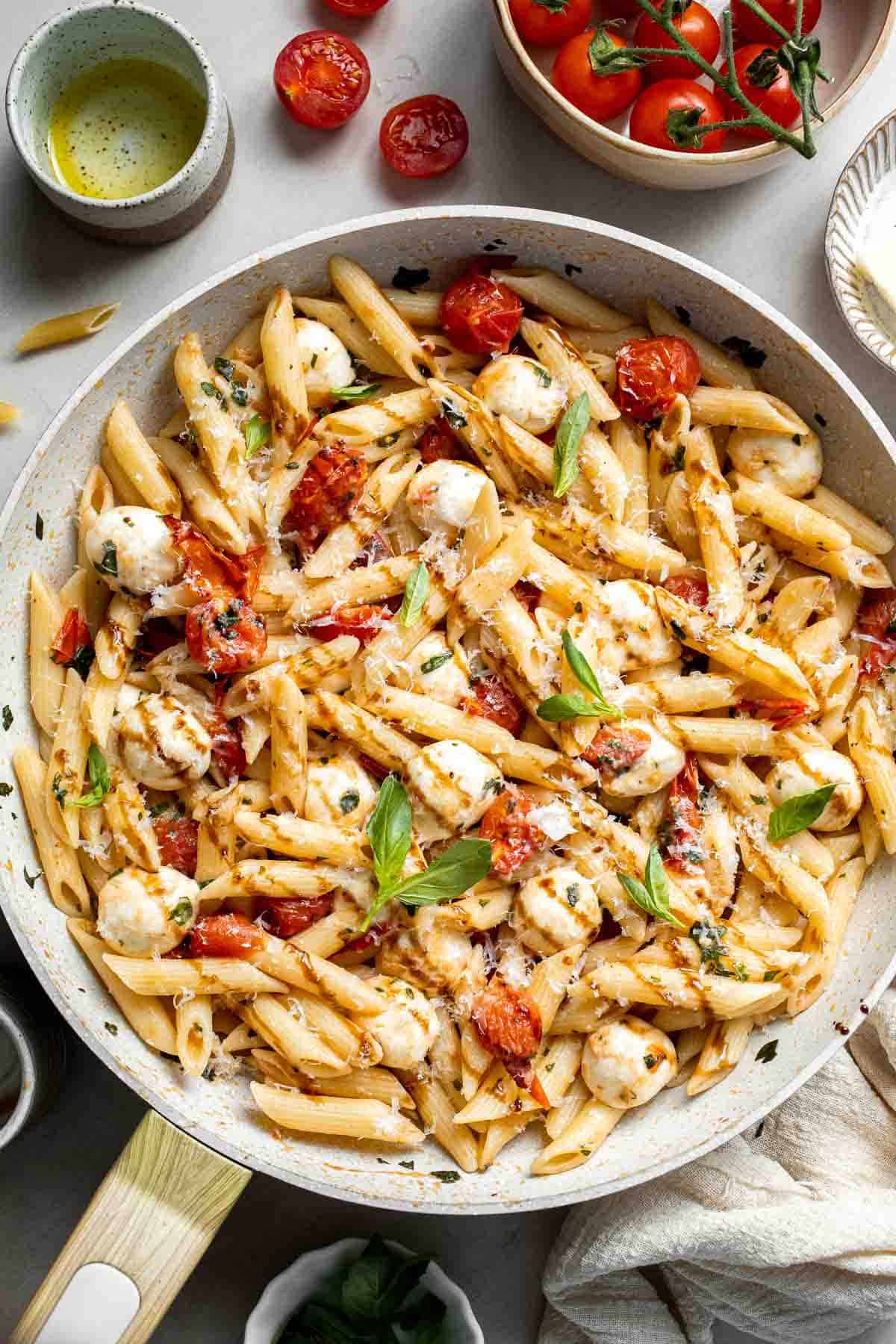 Caprese pasta served in a skillet with fresh mozzarella, basil, and cherry tomatoes.