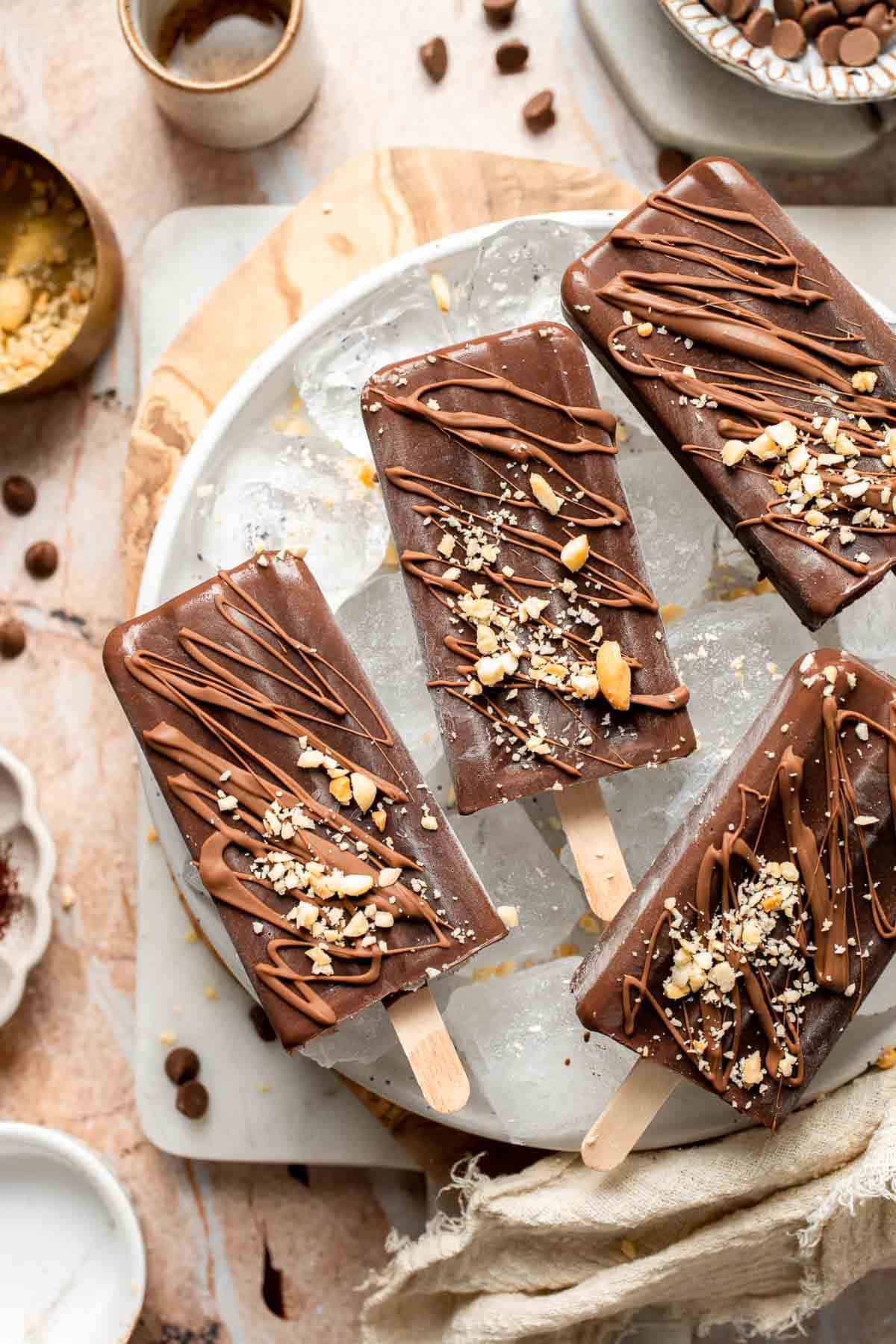 Homemade fudgesicles topped with melted chocolate and chopped nuts.