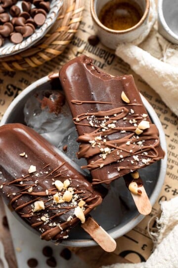 Homemade fudgesicles drizzled with melted chocolate and topped with chopped nuts on a serving platter.