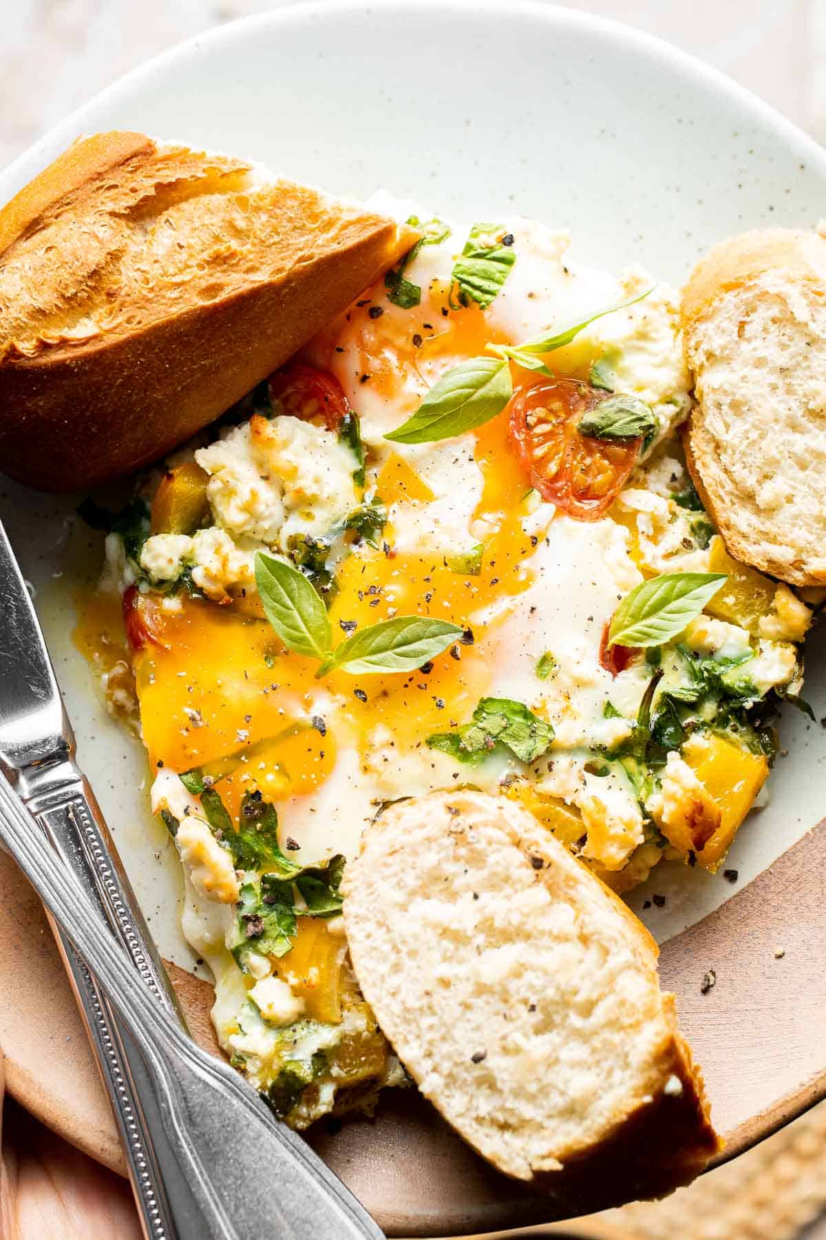 Serving of Mediterranean baked eggs with feta, vegetables, and toasted bread.