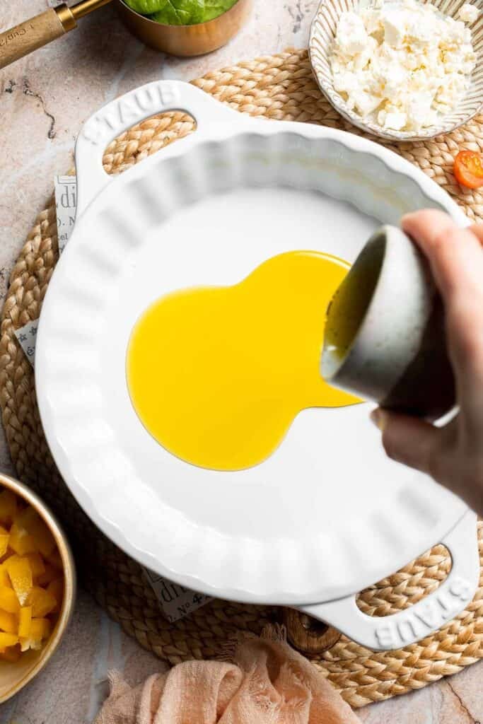 Olive oil being poured into a casserole dish for baked eggs.