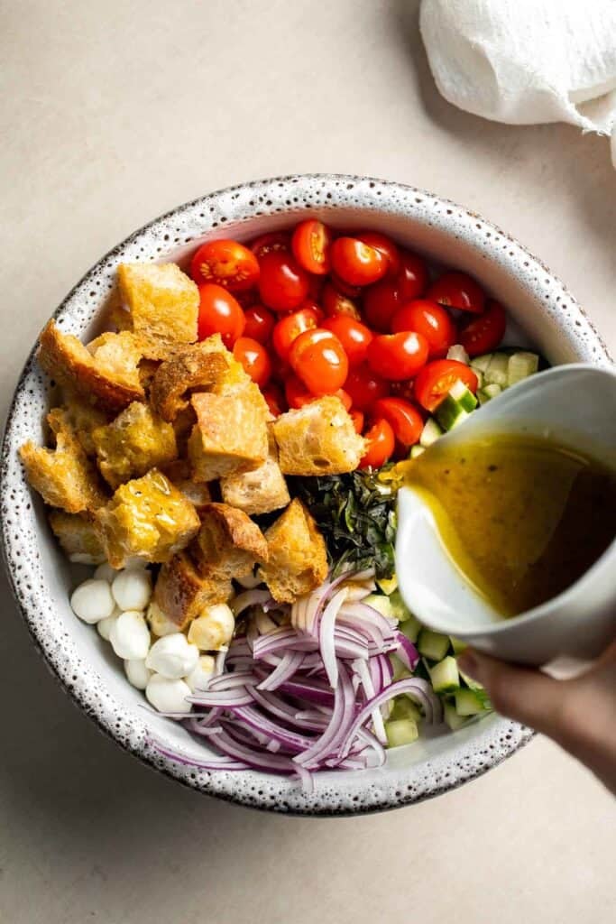 Pouring homemade vinaigrette over panzanella salad ingredients
