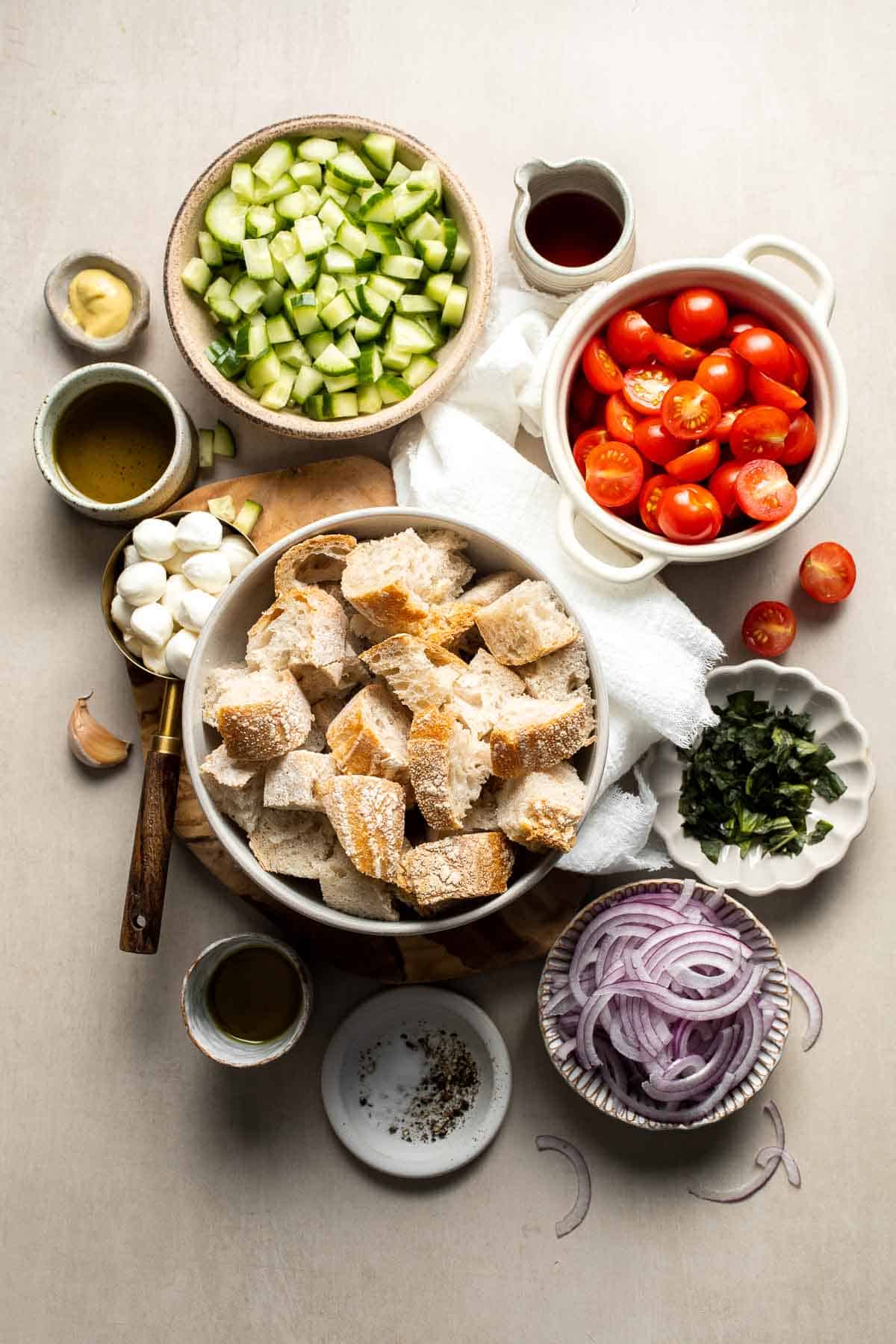 Ingredients for panzanella salad including bread, tomatoes, cucumber, red onion, mozzarella, and basil