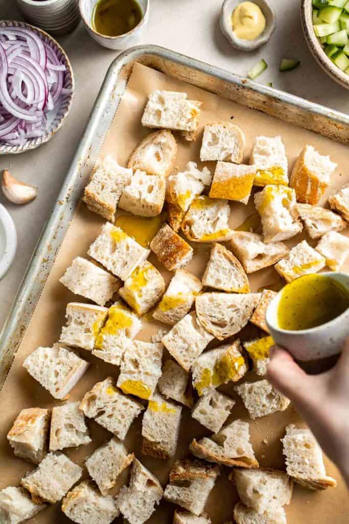 Bread cubes with olive oil drizzle on a baking sheet for panzanella salad