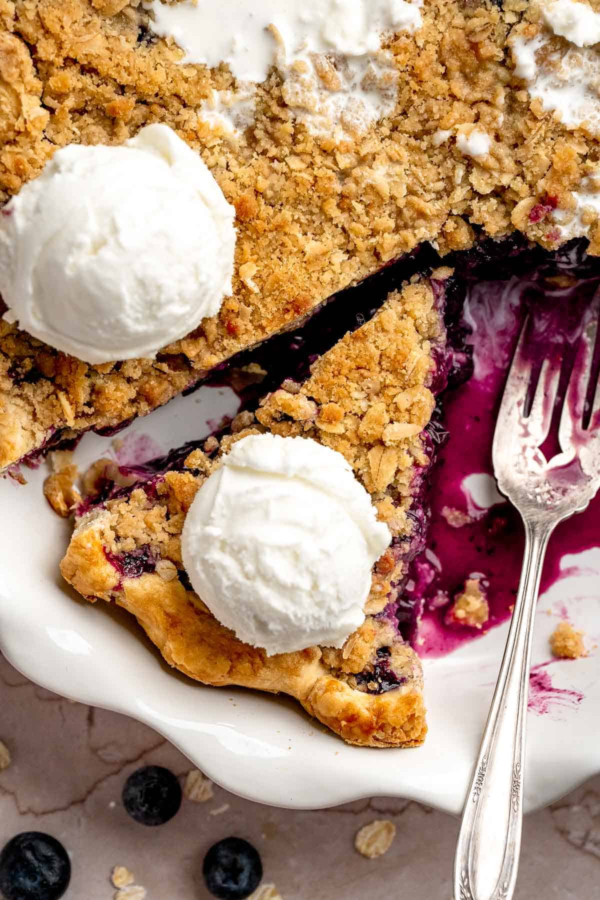 Slice of blueberry crumble pie topped with vanilla ice cream.