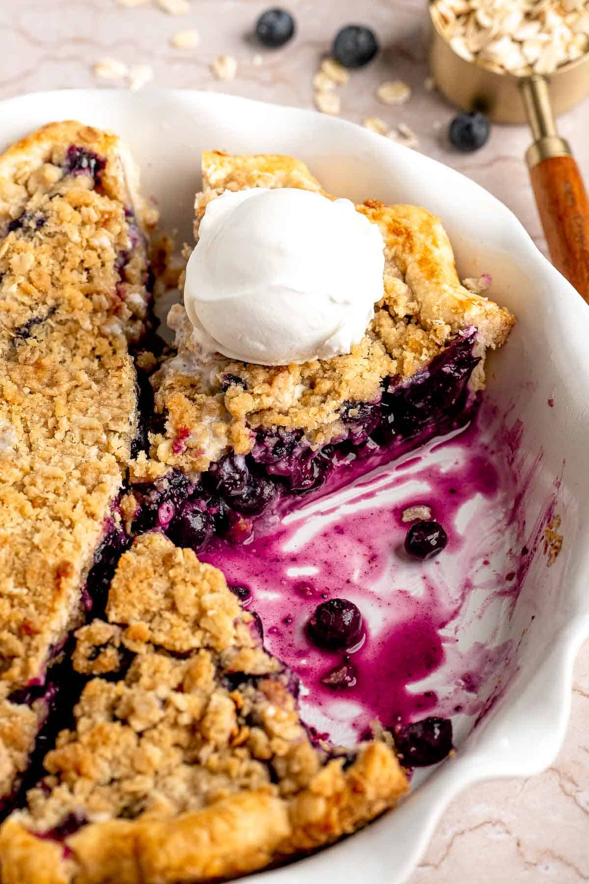 Close up of blueberry crumble pie with juicy blueberry filling and vanilla ice cream.
