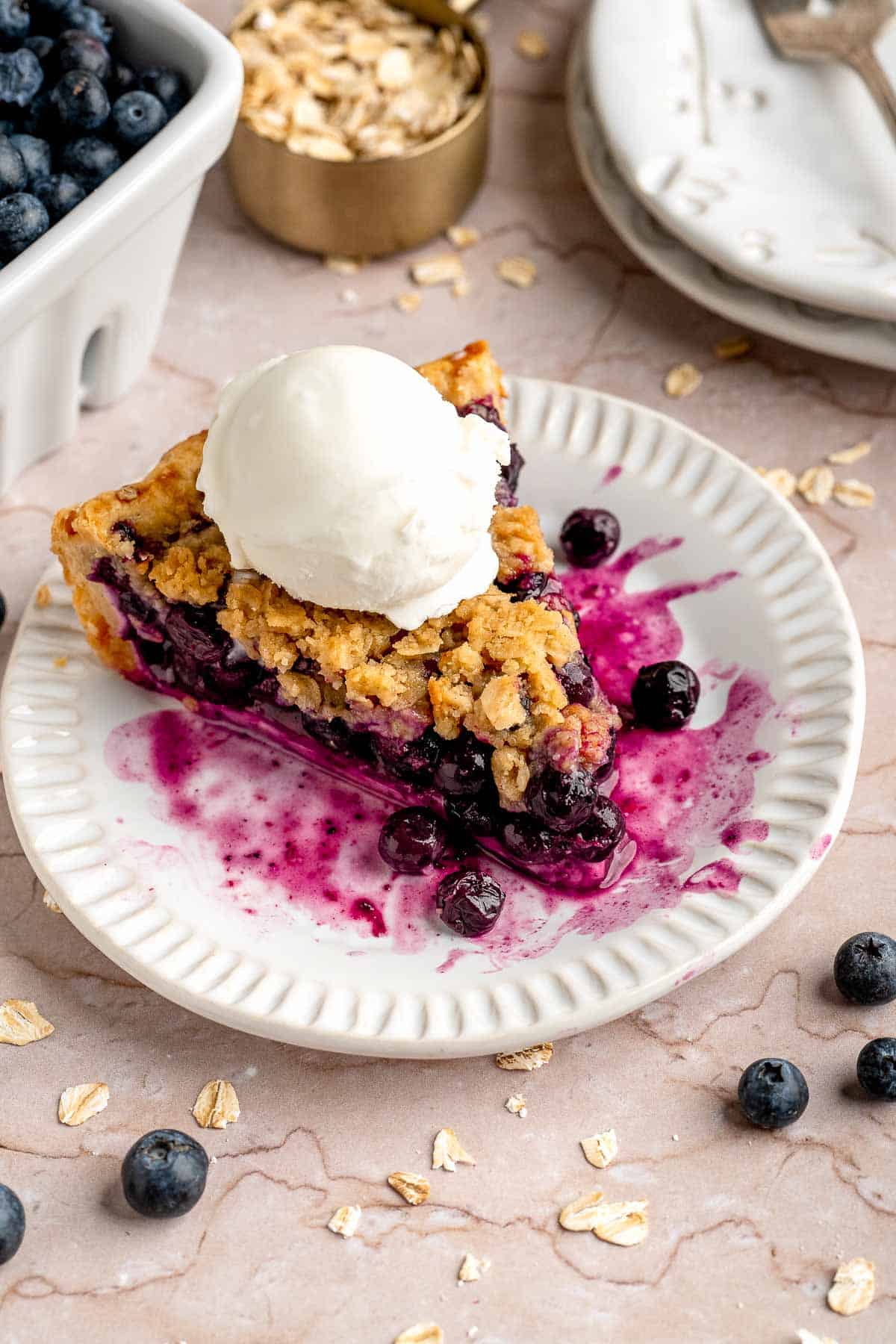 Slice of homemade blueberry crumble pie served on a dessert plate with vanilla ice cream.