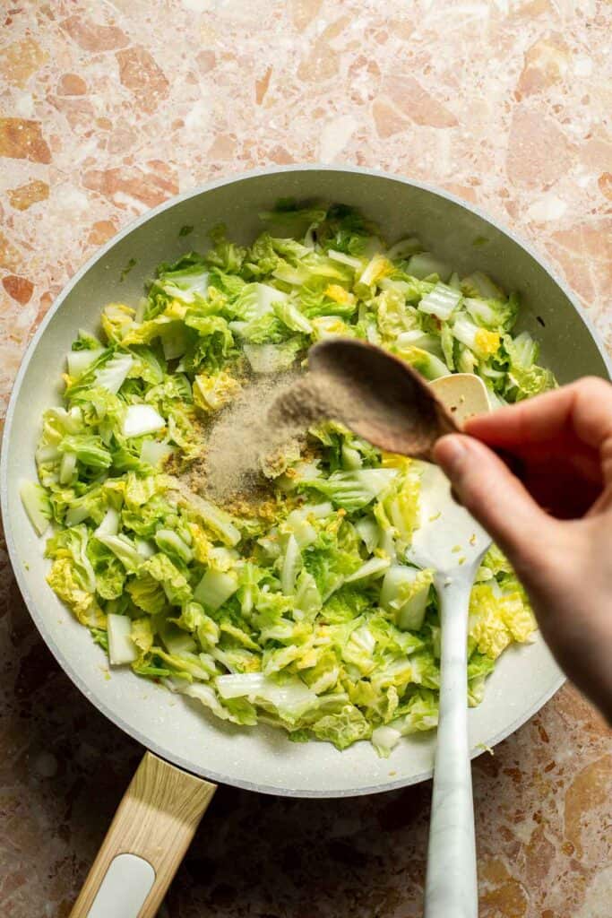 Chicken boullion powder and white pepper being added to cabbage while making Chinese Cabbage Stir Fry.