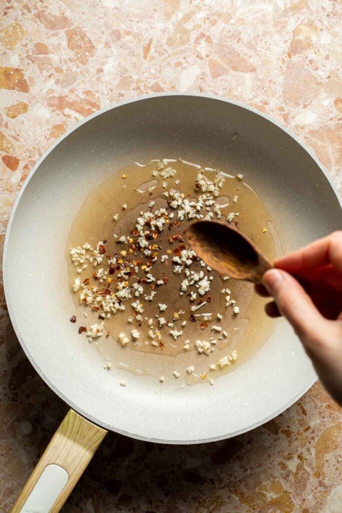 Adding garlic and chili flakes to oil in a skillet for Chinese Cabbage Stir Fry.