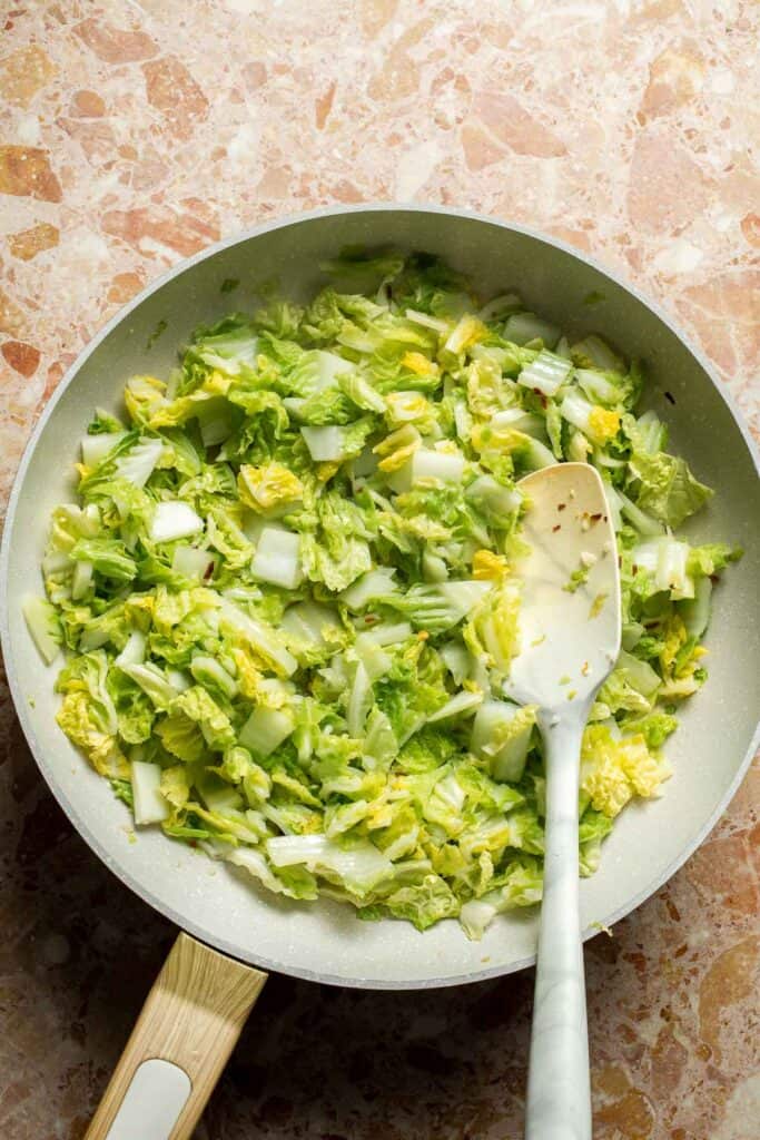 Napa cabbage cooking in a skillet until beginning to soften.