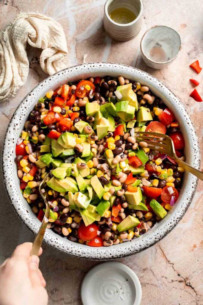 Adding diced avocado to Cowboy Caviar before gently mixing.