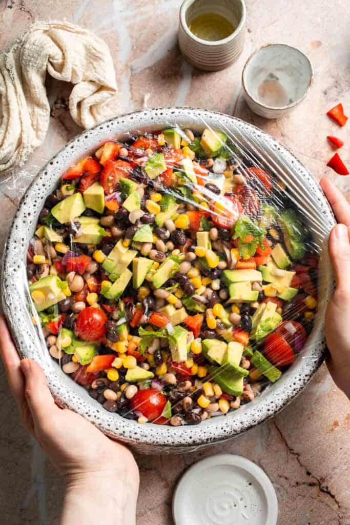 Covering Cowboy Caviar with plastic wrap before chilling in the refrigerator.