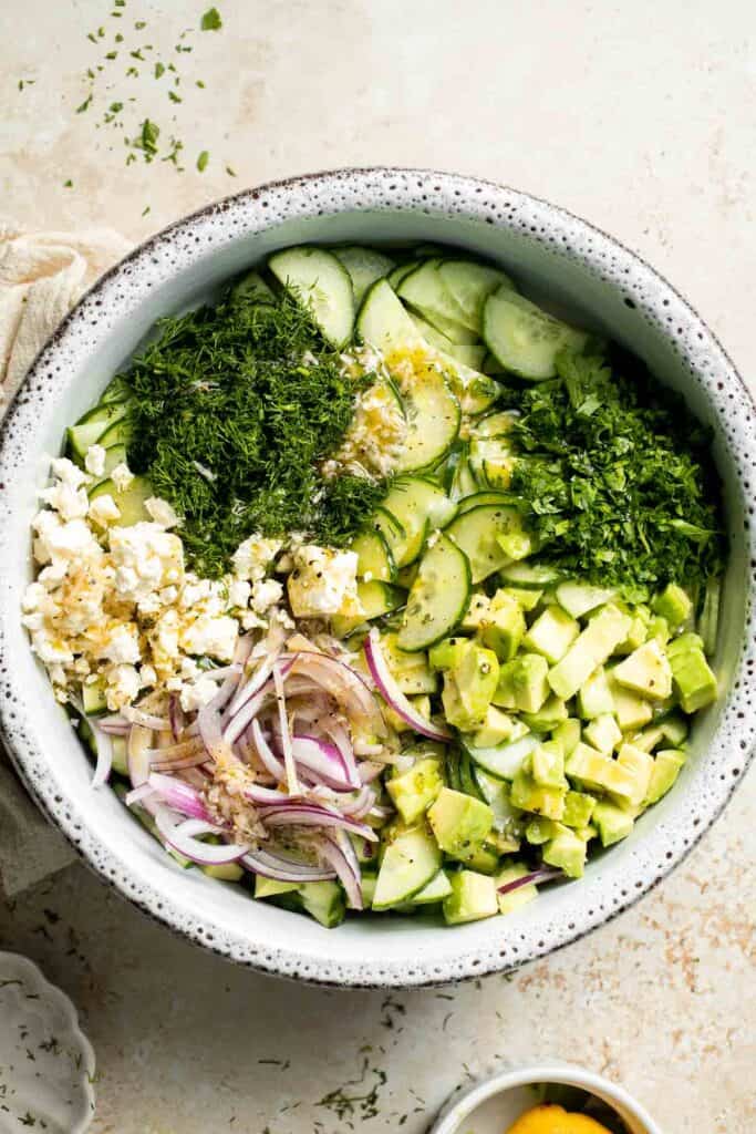 Cucumber feta salad ingredients with lemon dressing added before tossing.