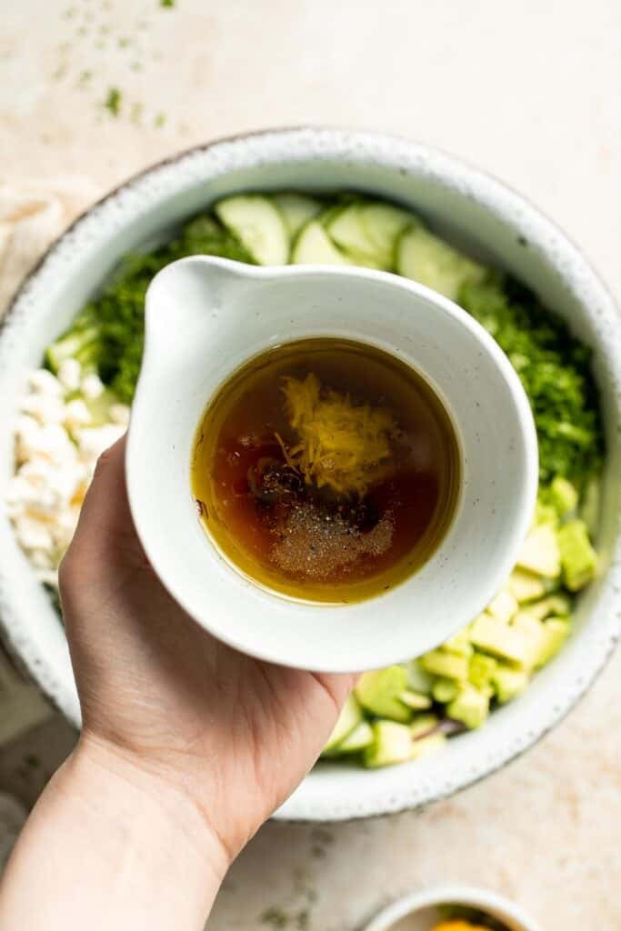 Olive oil, lemon juice, red wine vinegar, and grated garlic added to a bowl for cucumber salad dressing.