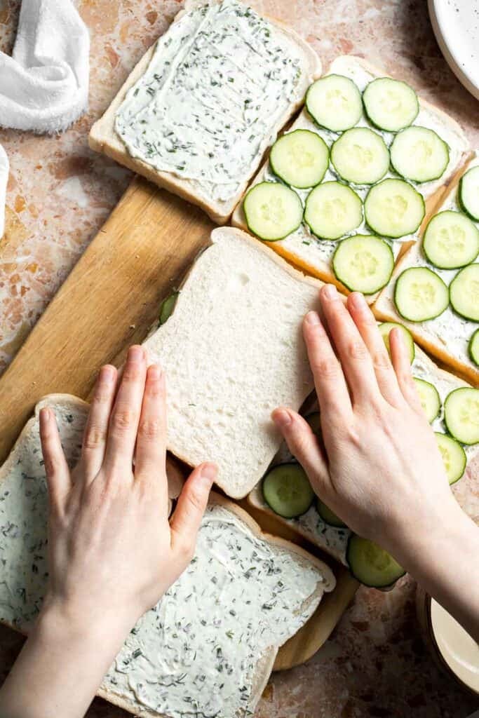 Placing bread over the cucumber slices to assemble Cucumber Tea Sandwiches.