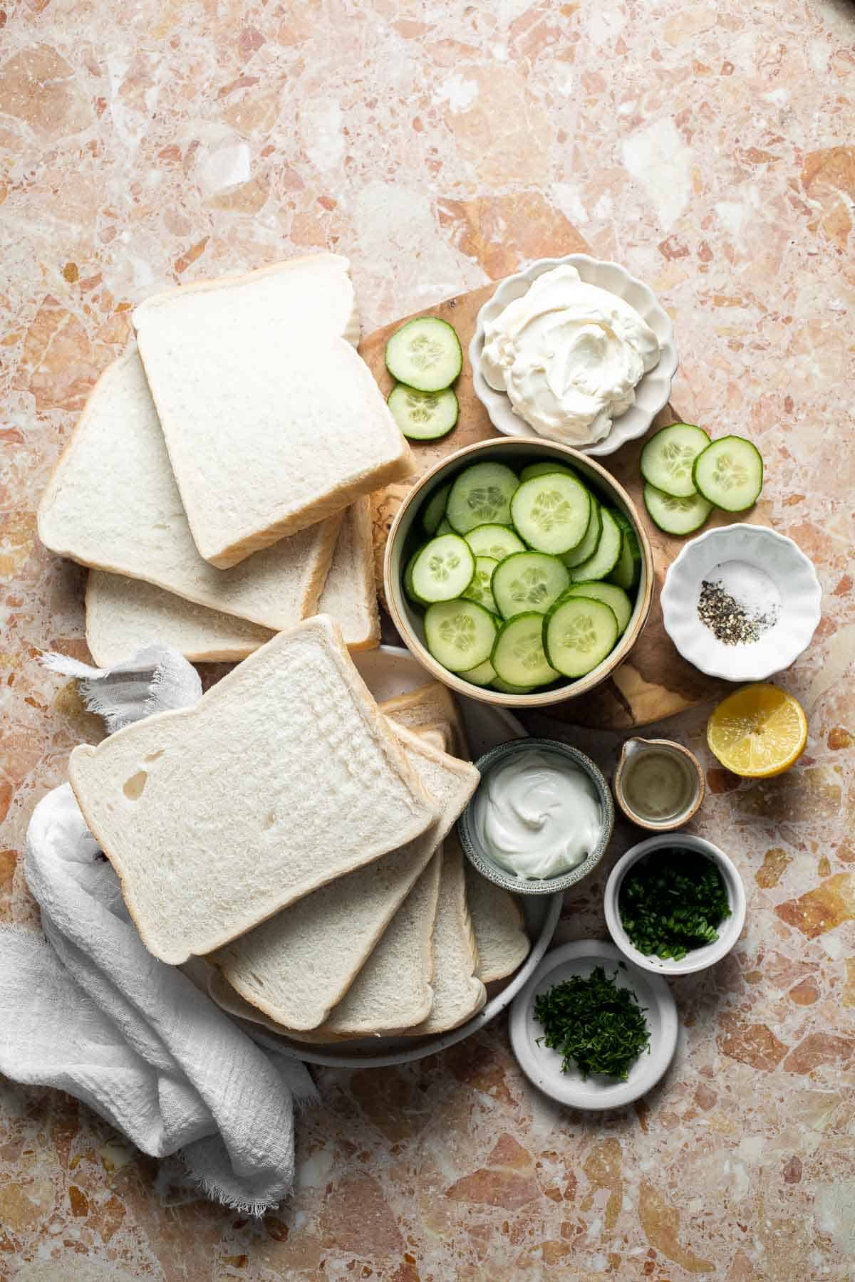 Ingredients for Cucumber Tea Sandwiches including white bread, sliced cucumber, cream cheese, fresh herbs, and seasonings.