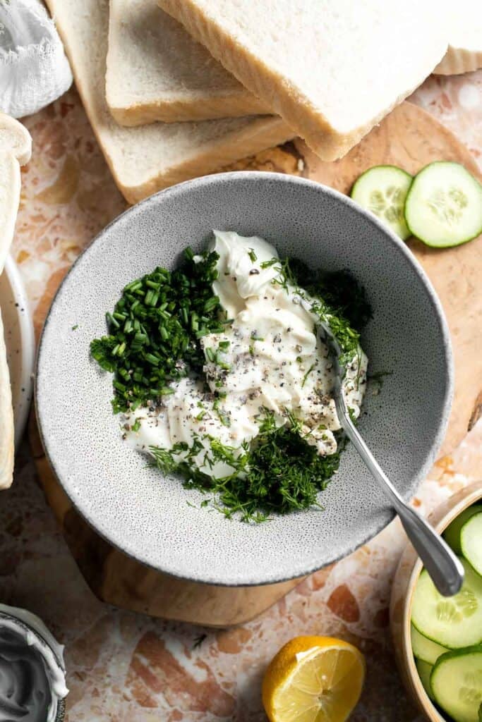 Cream cheese, mayonnaise, fresh dill, and chives in a bowl for making cucumber sandwich spread.
