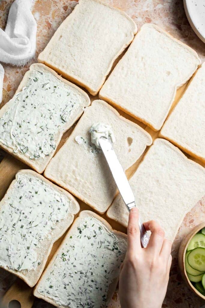 Spreading the cream cheese and herb mixture evenly over slices of white bread.