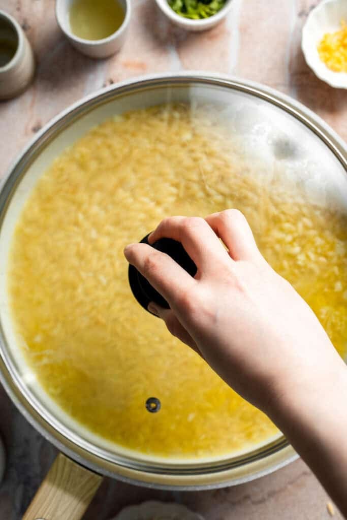 Covering orzo simmering in broth until tender and creamy.