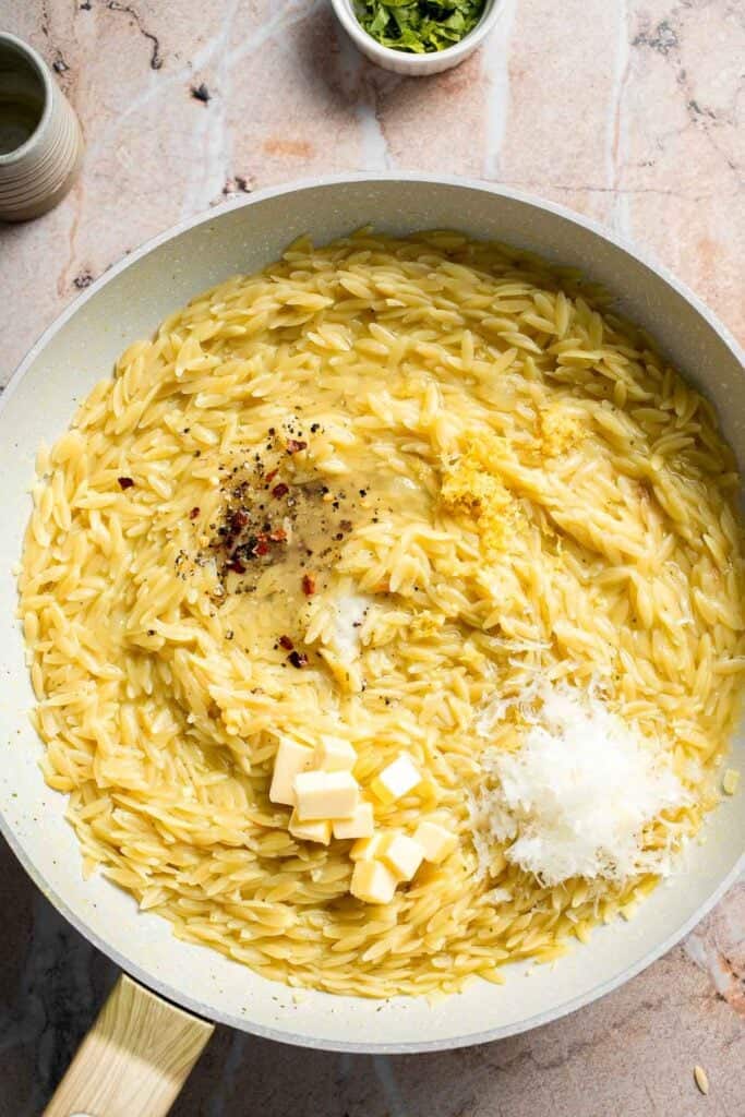 Adding butter, grated Parmesan, and seasonings to cooked orzo.