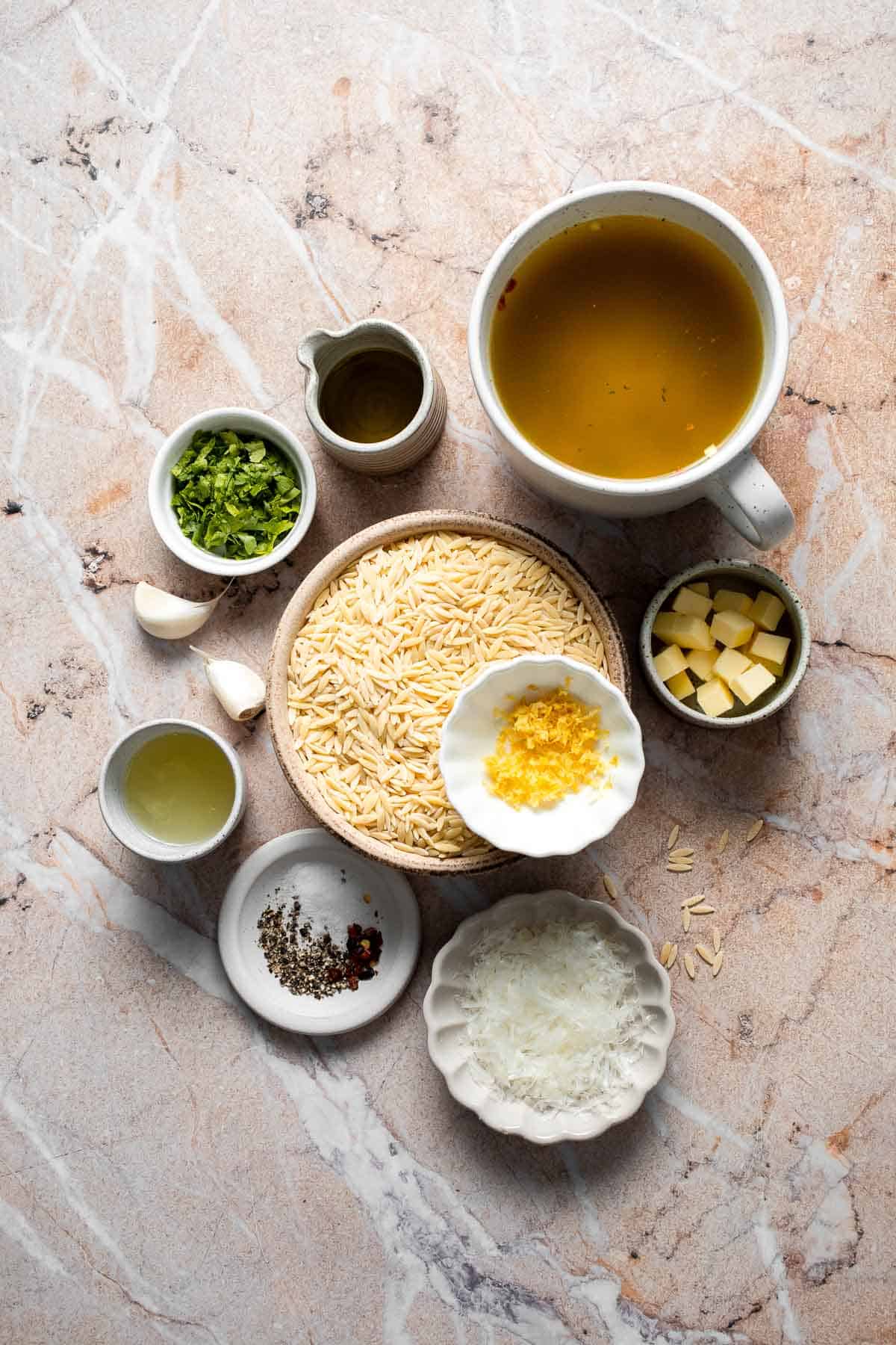 Ingredients for Lemon Orzo including dry orzo, vegetable broth, Parmesan cheese, garlic, butter, lemon, parsley, olive oil, and seasonings.
