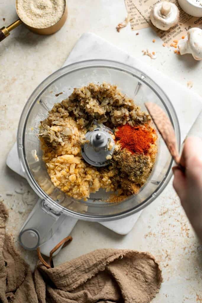 Adding seasoning to the red lentil patty mixture in a food processor.