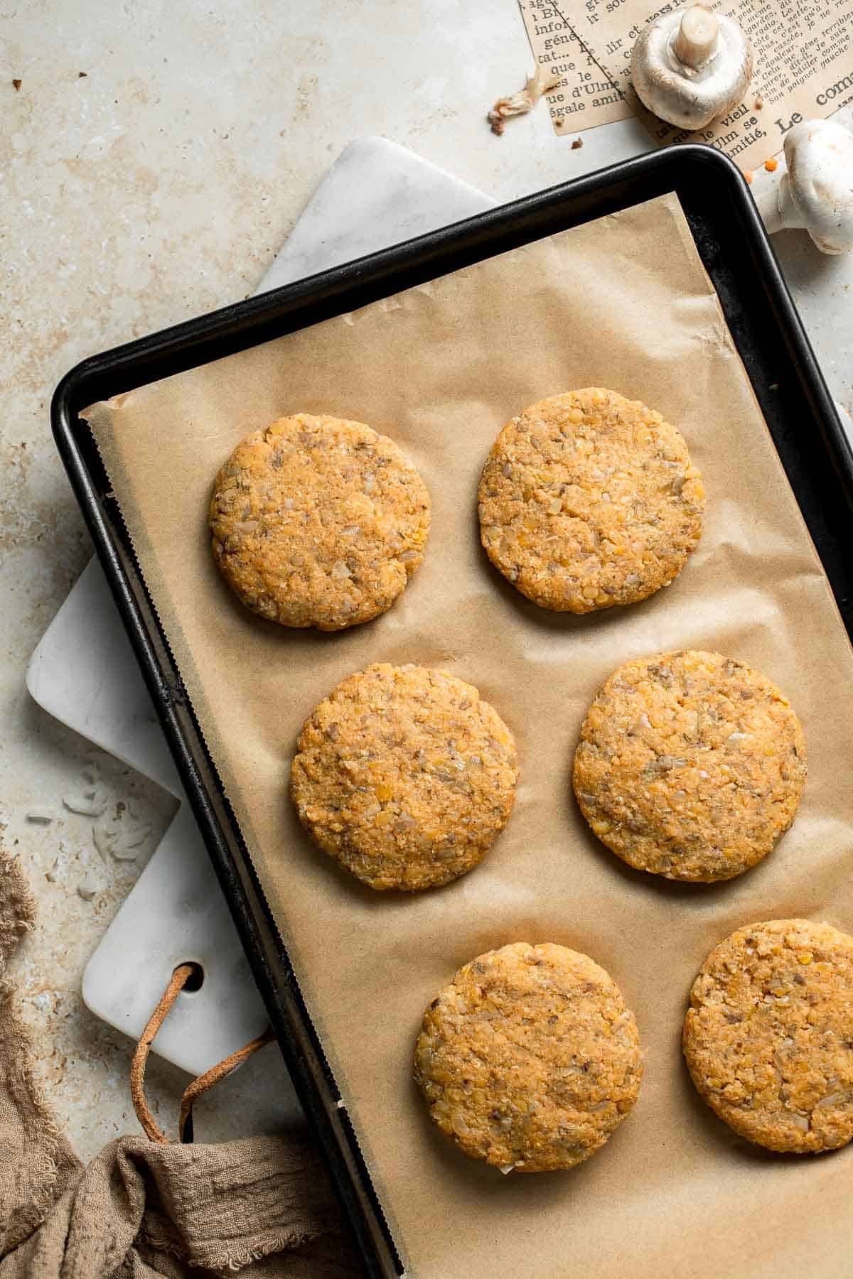 Shaped red lentil patties arranged on a parchment-lined baking sheet.