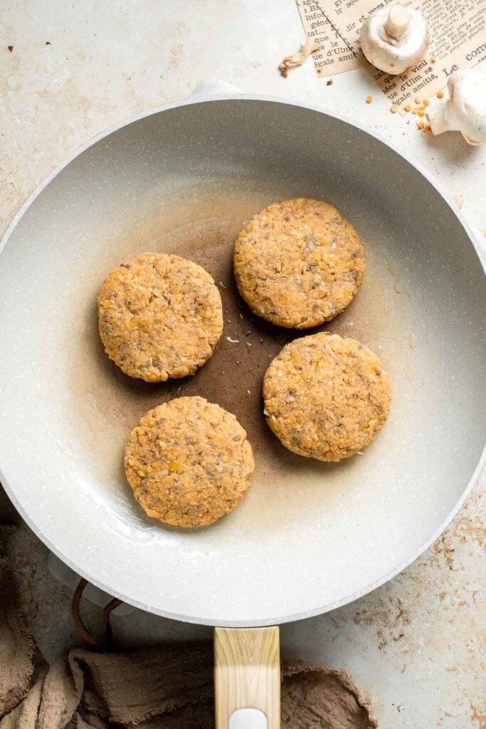 Uncooked lentil patties arranged in a skillet for pan frying.