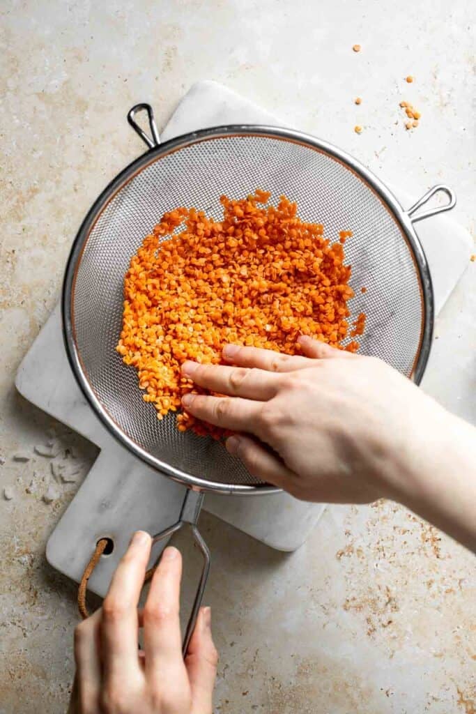 Rinsing uncooked red lentils in a fine mesh strainer.